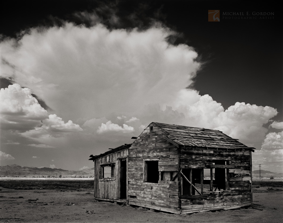 An abandoned historic shack in California's Mojave Desert framed by a towering cumulonimbus thunderstorm cloud.Logos and watermarks...