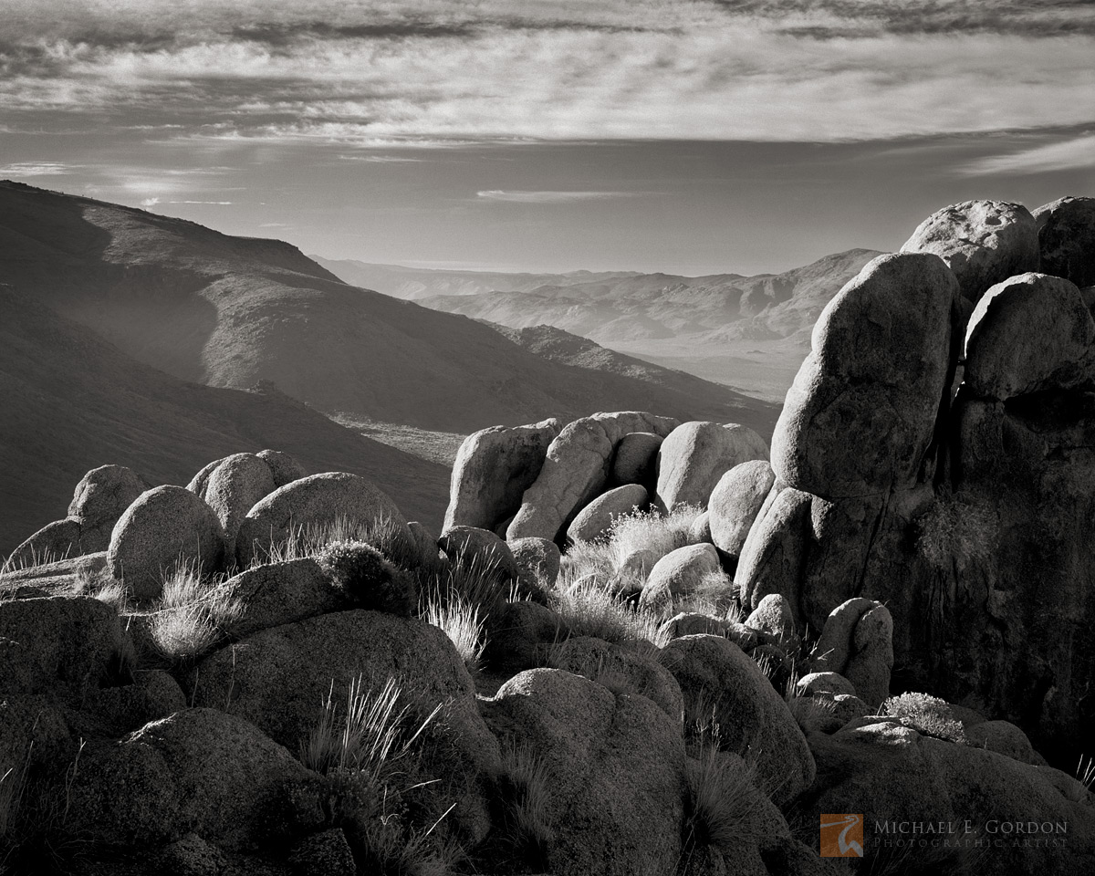 Morning light illuminates granite and shrubs high on a mountain ridge.&nbsp;