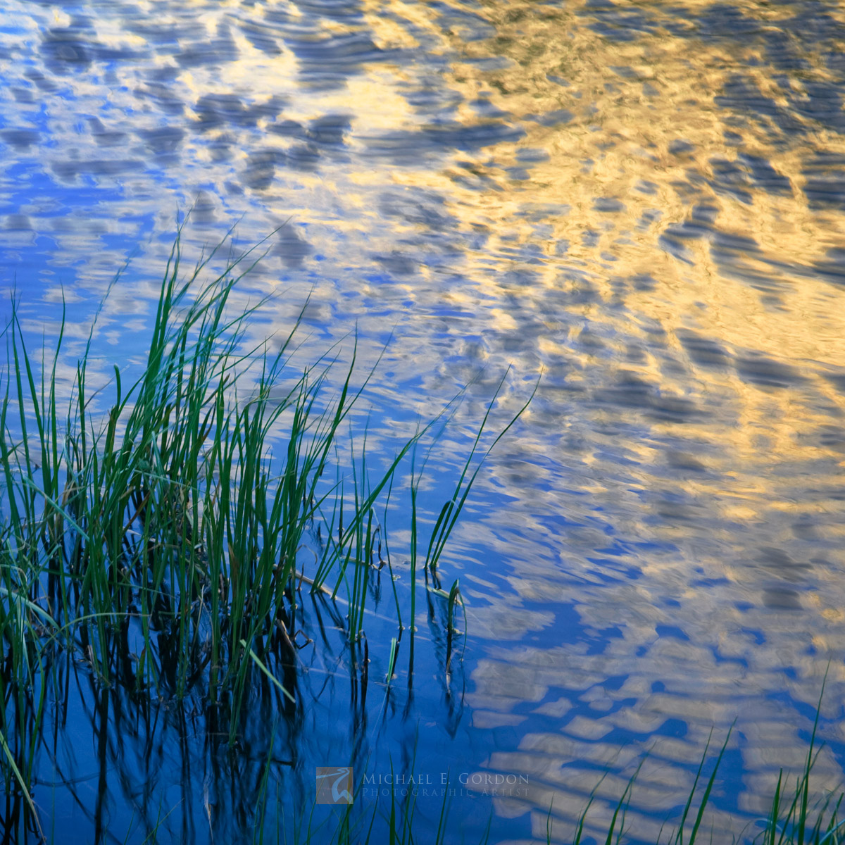 Golden High Sierra granite at sunrise reflects on a&nbsp;wind-rippled pond. Logos and watermarks are not found on any printed...