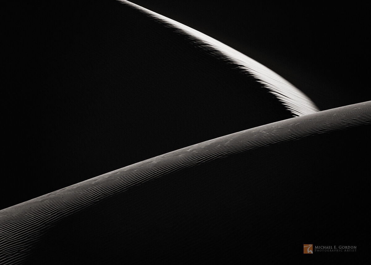 An abstract photograph from Death Valley's Mesquite Sand Dunes, resembling edge lit planets in space.