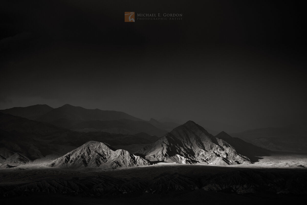 Dramatic storm light enters from a dark stage right to illuminate Death Valley Buttes, Death Valley National Park.