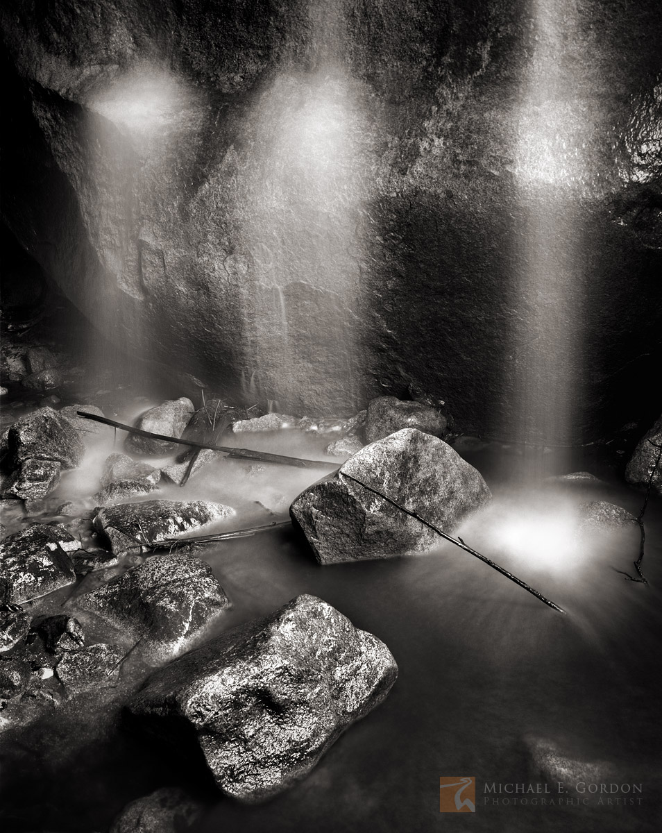 Three slender veils of falling water resemble ghosts in a dimly lit subterranean canyon grotto.&nbsp;Logos and watermarks are...